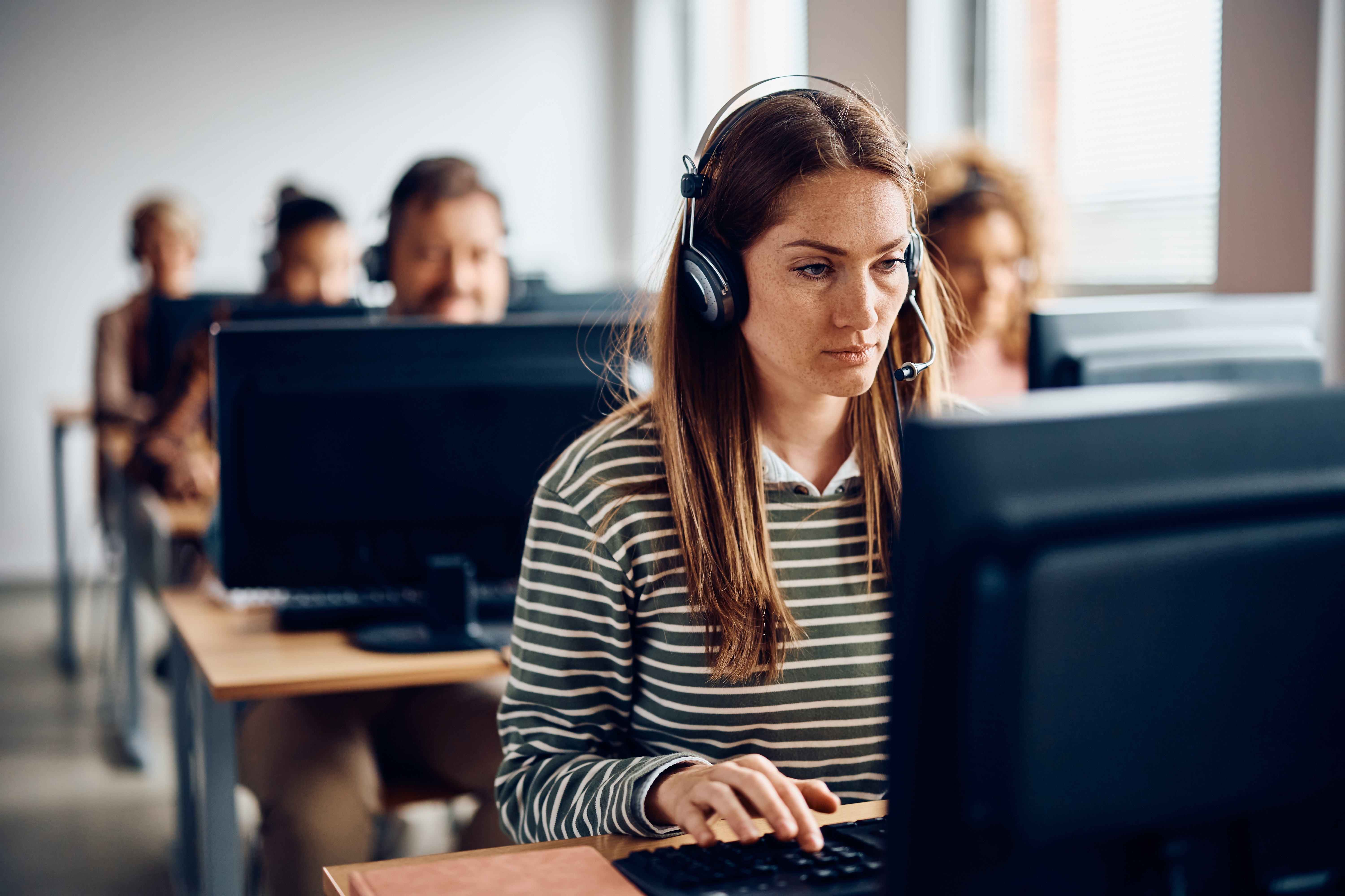 U računalnoj učionici vidimo studente svakog za jednim računalom i slušalicama s mikrofonom.