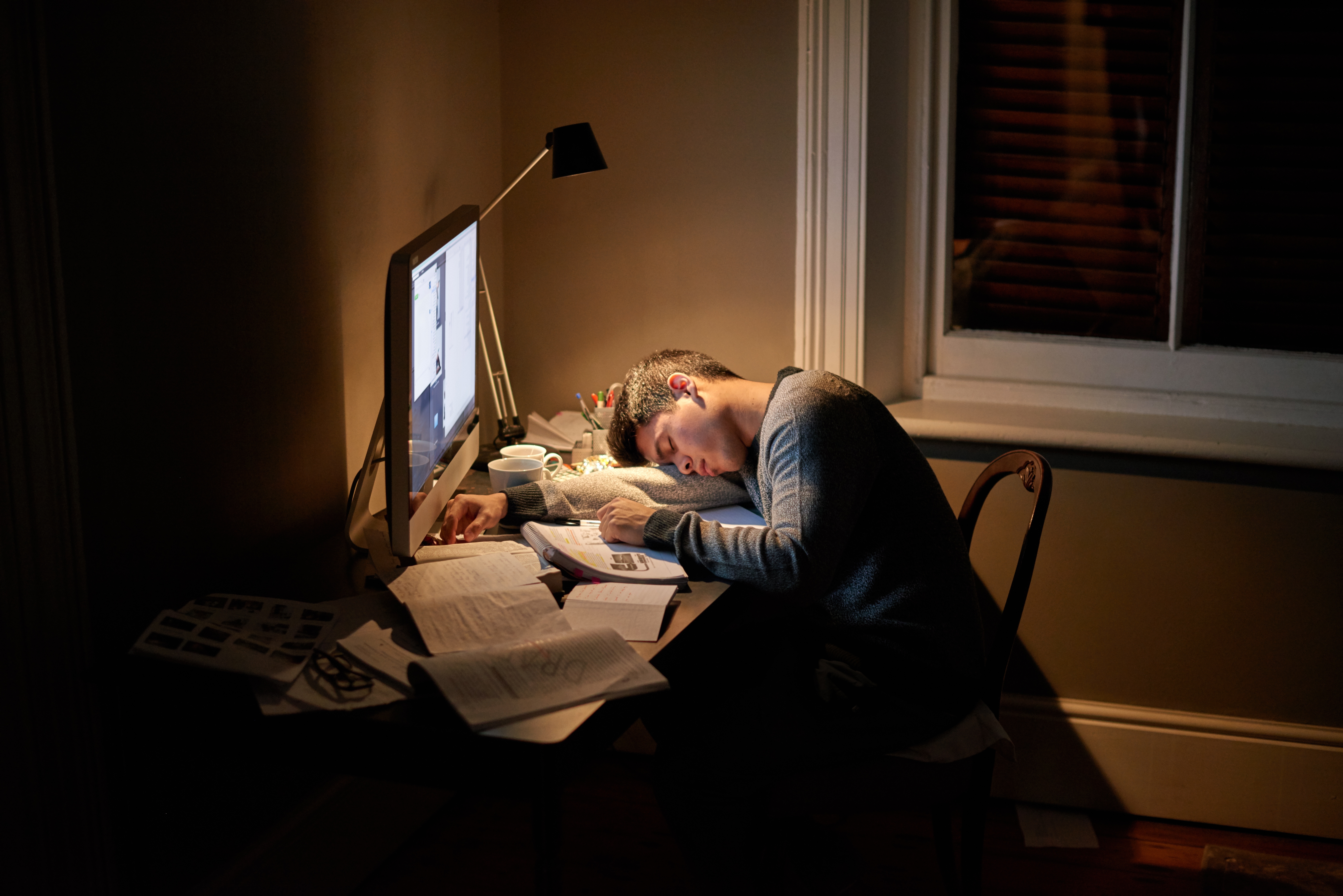 Student za radnim stolom kasno kod kuće leži na knjigama i bilježnici zbog nedostatka vremena ranije u danu i drugih obaveza.