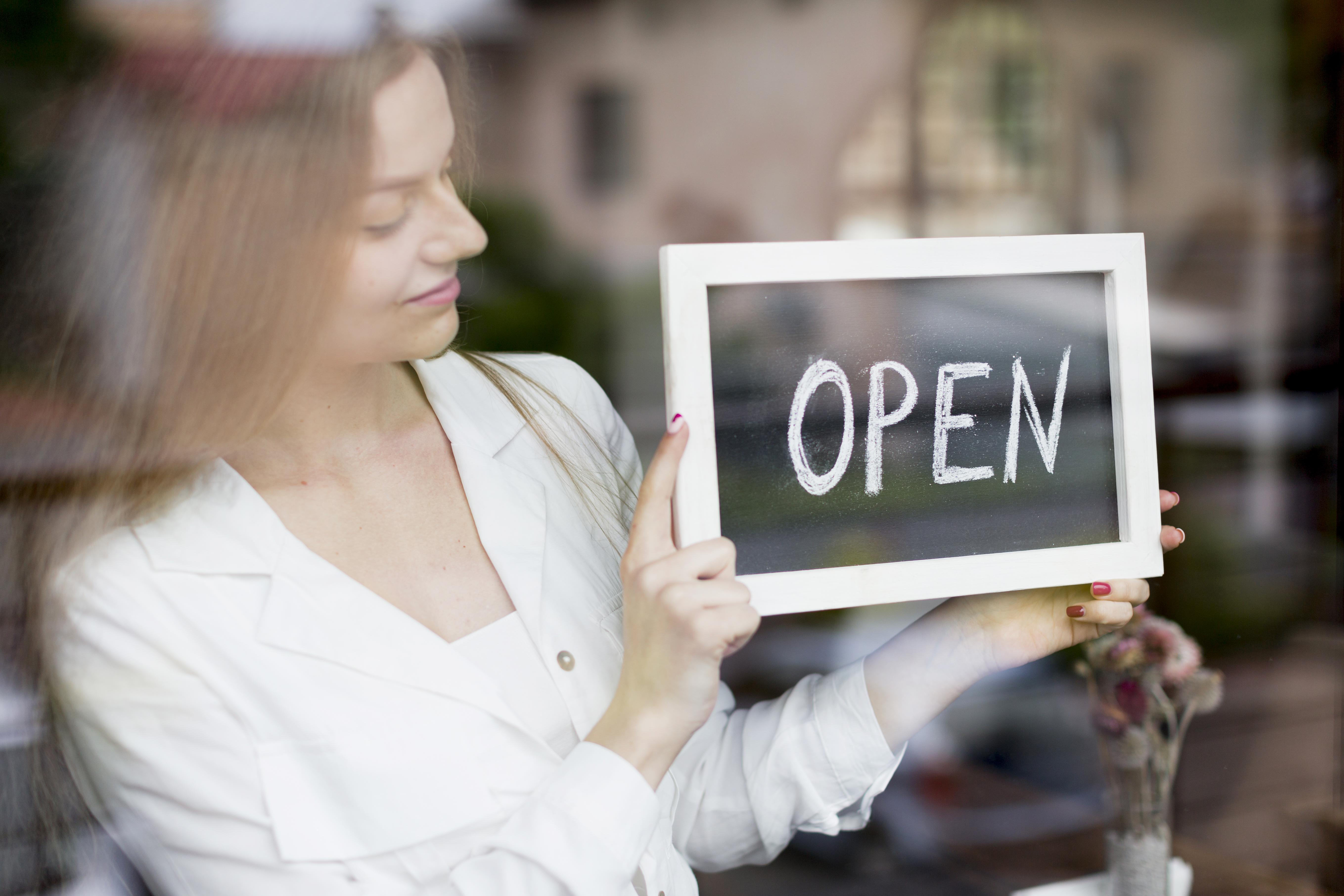 A female person holding a sign that says "OPEN"